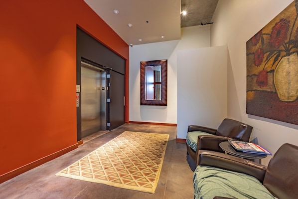 A hallway with a red wall, a patterned rug, a sofa, a table with a magazine, and a painting on the wall.