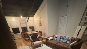 Una sala de estar con sofá, alfombra, mesa de comedor con sillas y una zona de cocina al fondo.