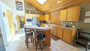 A modern kitchen with wooden cabinets, a central island with bar stools, and a dining area. - Red Cedar 53 (Bend)