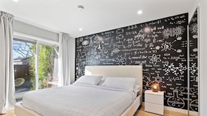 A bedroom with a large bed, a nightstand, and a wall covered in scientific equations and diagrams. - Marbella Lane - SJ Designer Home 3BR Ldry P (San Jose)