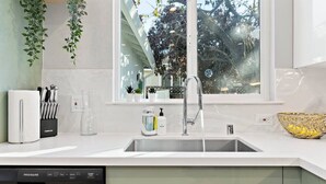 A modern kitchen with a stainless steel dishwasher, a sink with a faucet, and a window with a view of trees. - Marbella Lane - SJ Designer Home 3BR Ldry P (San Jose)