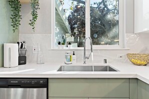 Una cocina moderna con lavavajillas de acero inoxidable, un fregadero con grifo y una ventana con vista a árboles.