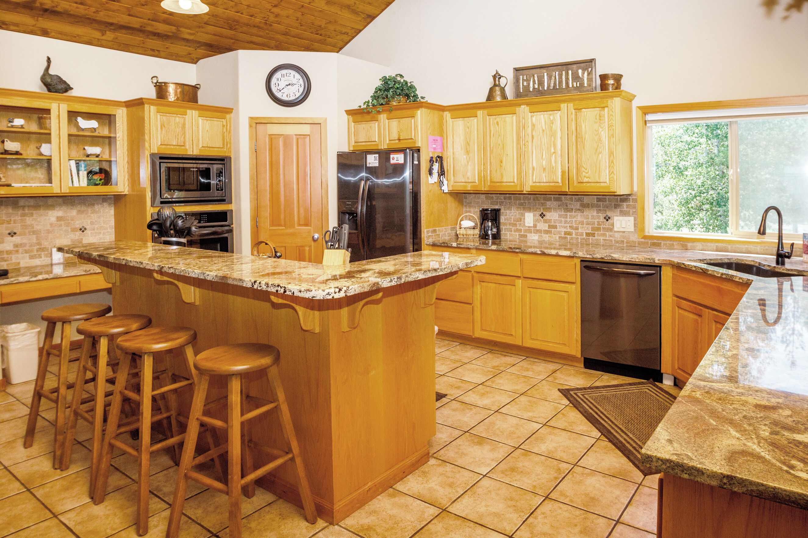 A spacious kitchen with wooden cabinets, a granite countertop, a stainless steel refrigerator, and a large island with bar stools.