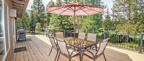 A wooden deck with a glass-top table and chairs, surrounded by a metal railing.