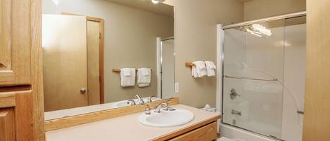 A bathroom with a vanity, sink, mirror, and shower.