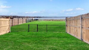 Uma área gramada cercada, com vista para um corpo d'água e edifícios ao longe.