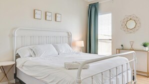 Cama bem arrumada com roupa de cama branca, mesa de cabeceira com abajur e espelho fixado na parede.