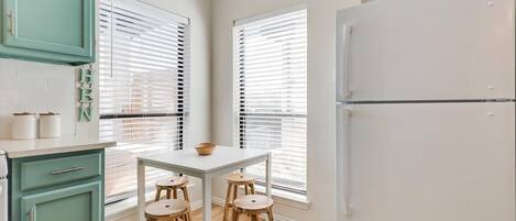Una cocina con una mesa blanca, taburetes de madera y un armario color turquesa.