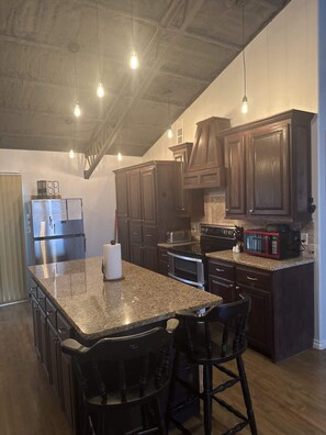 A kitchen with dark wood cabinets, a granite countertop, a stainless steel refrigerator, and a built-in oven.