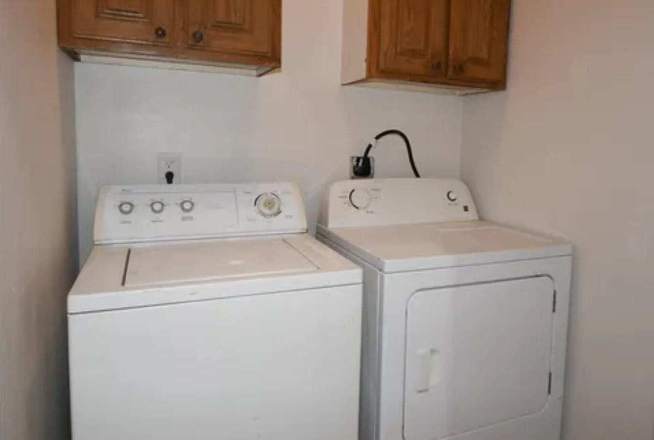 A laundry area with a washer and dryer, wooden cabinets above, and a power outlet on the wall.