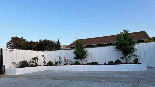 A residential backyard with a white fence, various shrubs, and a concrete patio. - Marbella Lane - Serene Haven Retreat 3BR (Ontario)