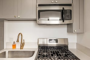 Una cocina con un microondas de acero inoxidable, estufa a gas y un grifo dorado.