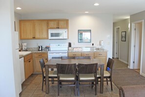 A modern kitchen with wooden cabinets, a microwave, and a dining area with a table and chairs. - 7th Mtn 923b (Bend)