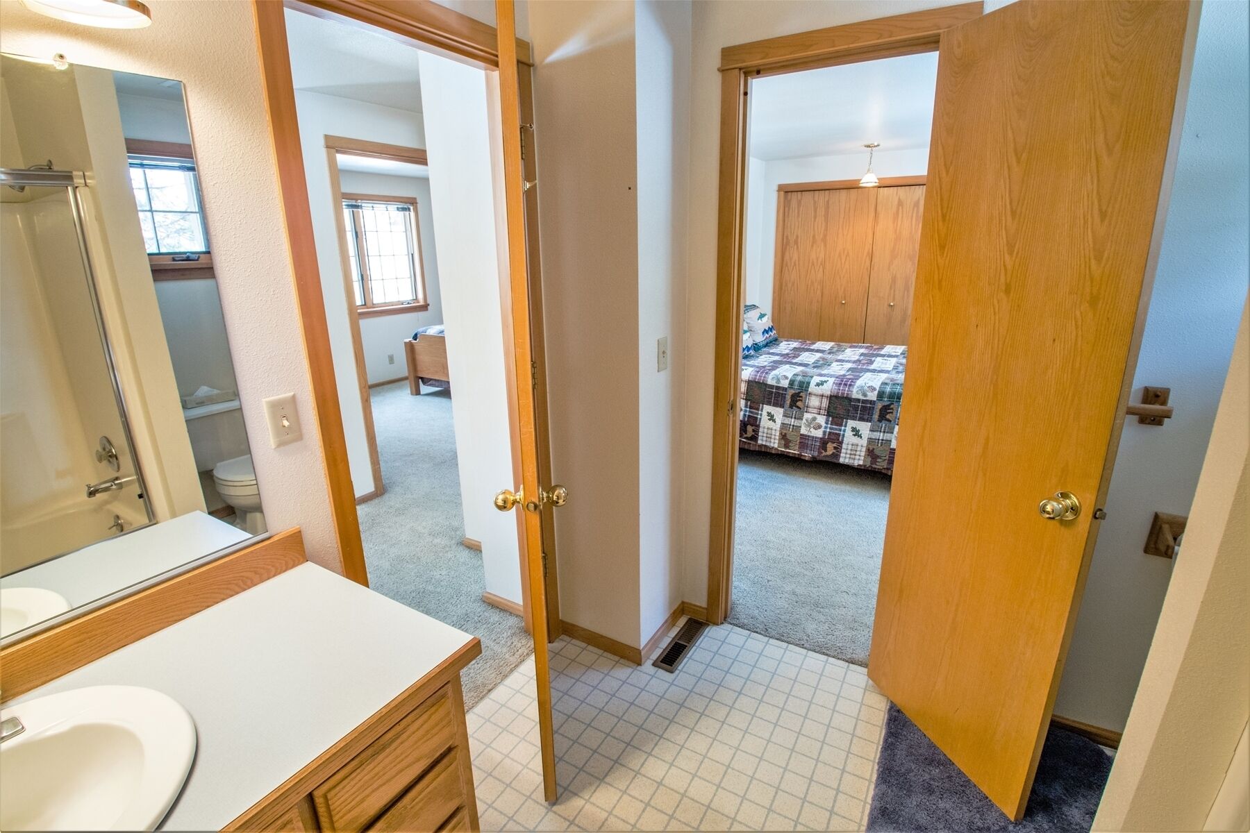 A bathroom with a sink and mirror, a hallway leading to a bedroom with a bed and a wardrobe.