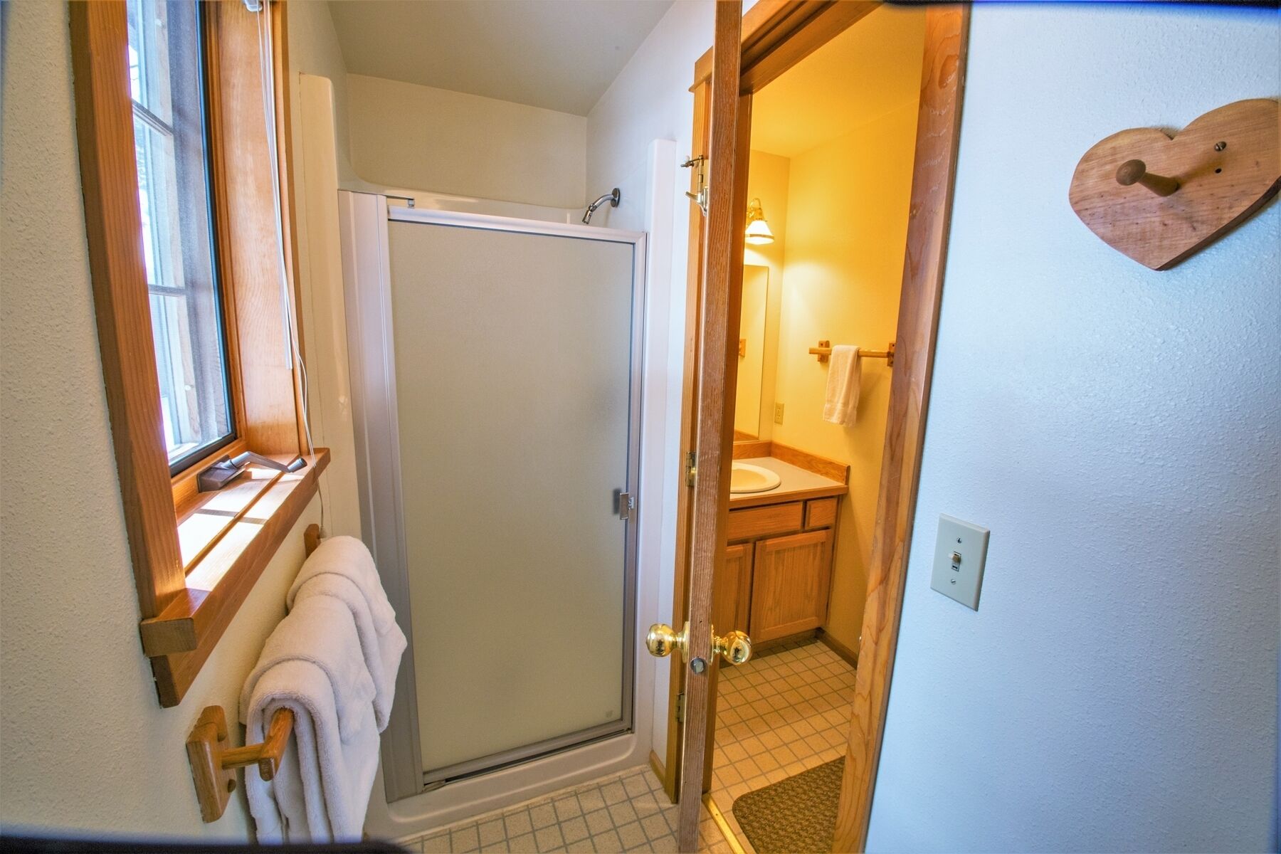 A bathroom with a shower, toilet, and sink. There is a towel rack with towels, a wooden door, and a light fixture above the sink.