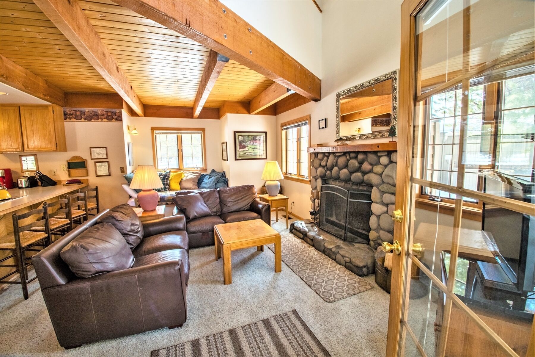 A cozy living room with a fireplace, leather sofas, a dining area, and wooden beams on the ceiling.