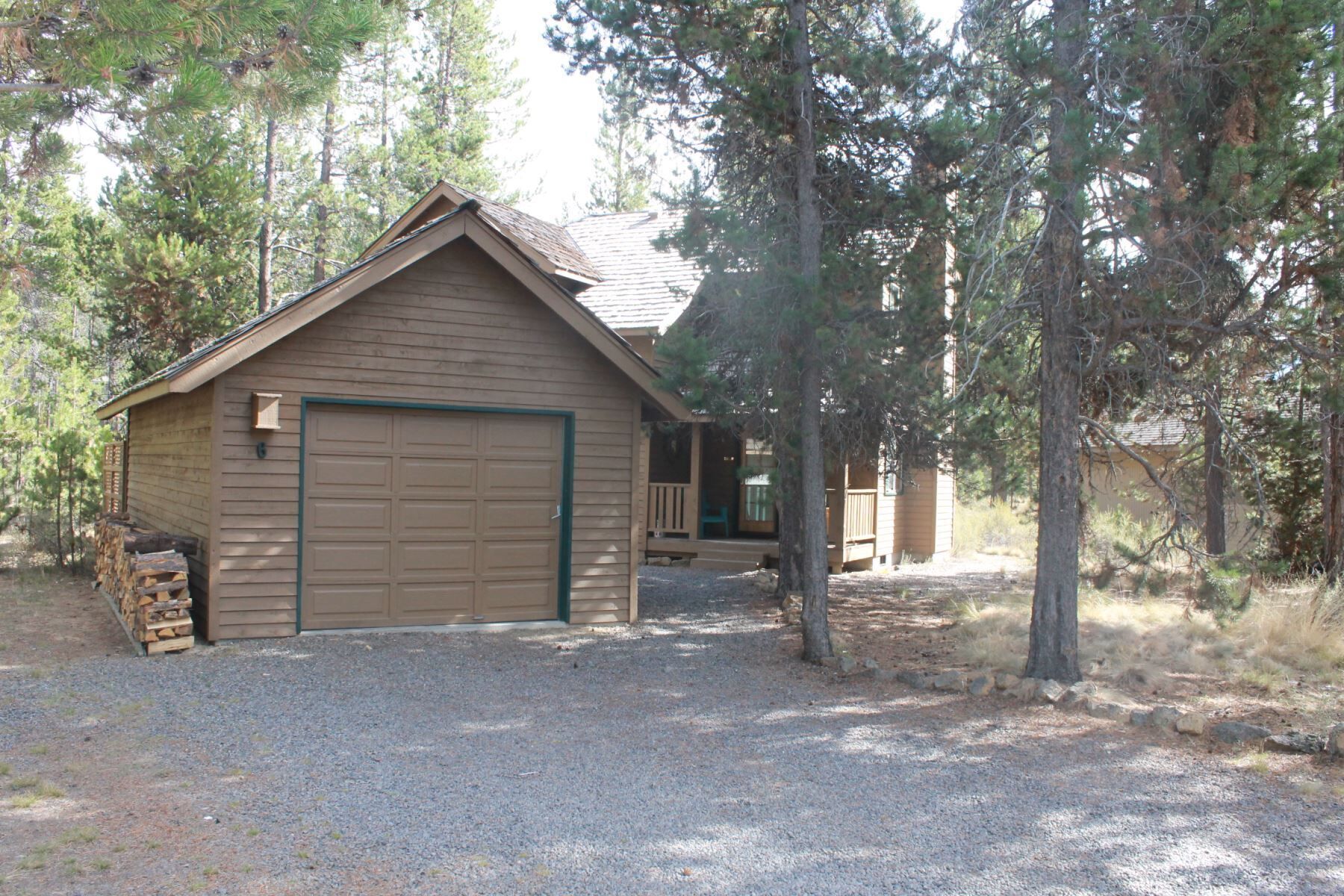 A wooden cabin with a garage, surrounded by trees.