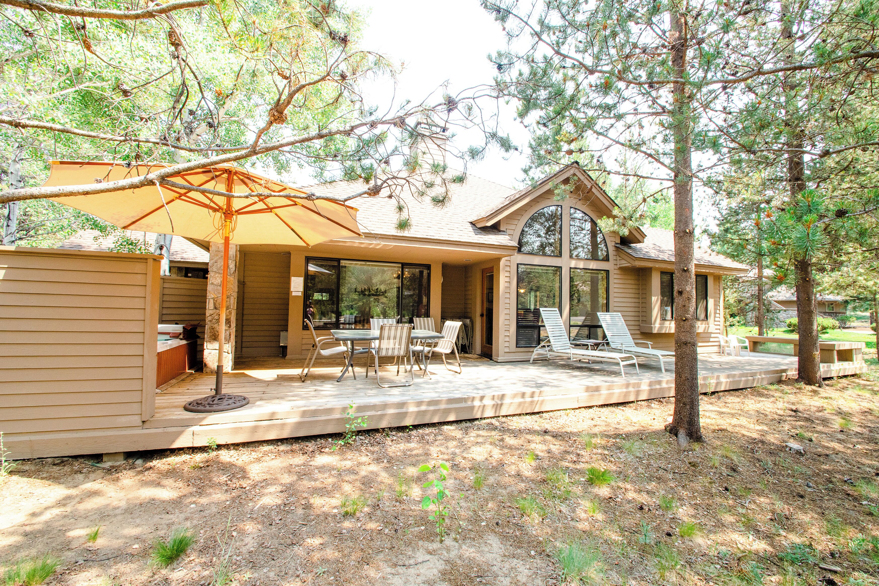A house with a patio area featuring a table and chairs, an umbrella, and a view of the surrounding trees.
