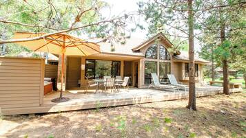A house with a patio area featuring a table and chairs, an umbrella, and a view of the surrounding trees.