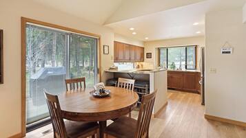 A dining area with a round wooden table and chairs, a kitchen with wooden cabinets, and a large window with blinds.