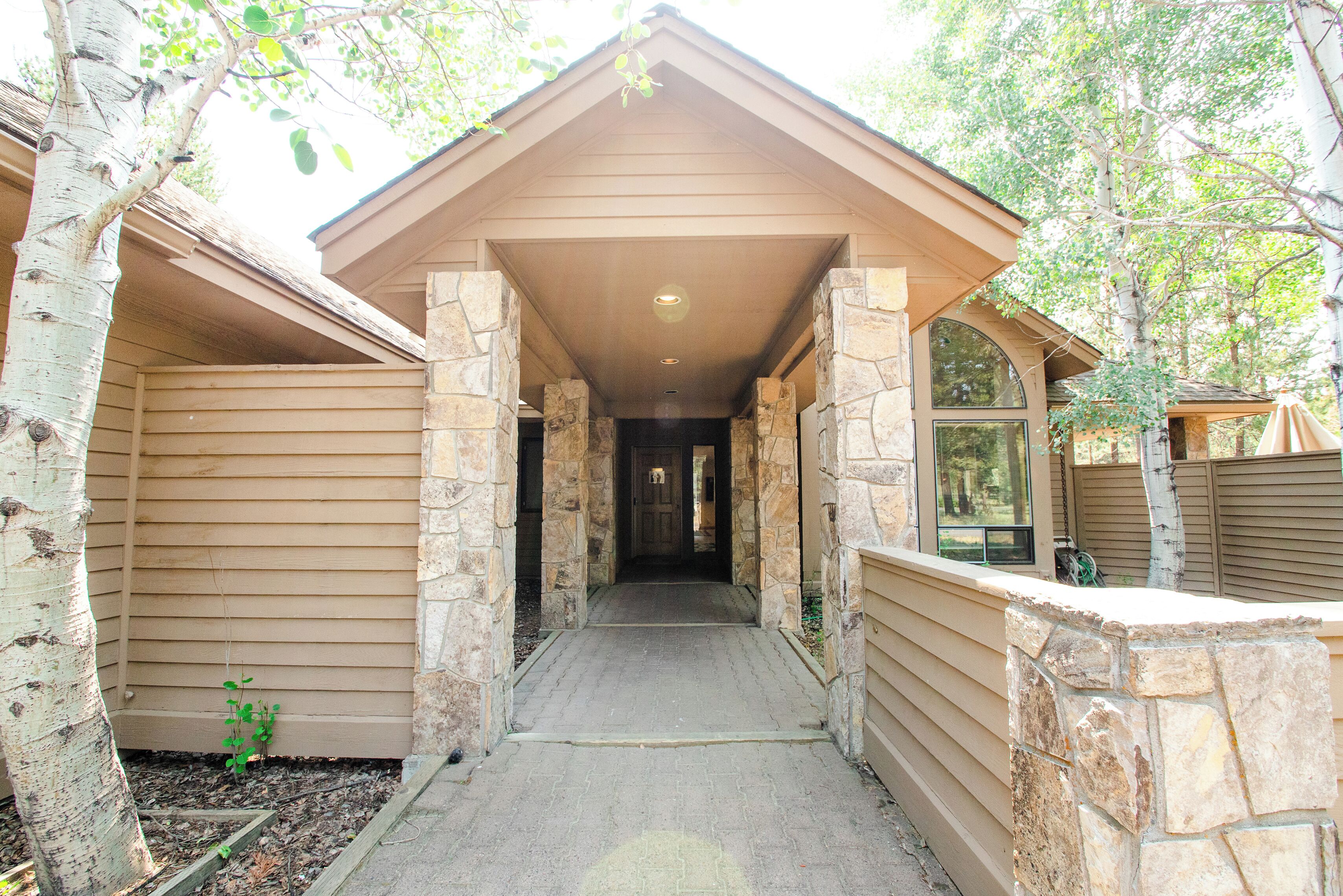 A covered walkway leading to a building with stone pillars and wooden siding.
