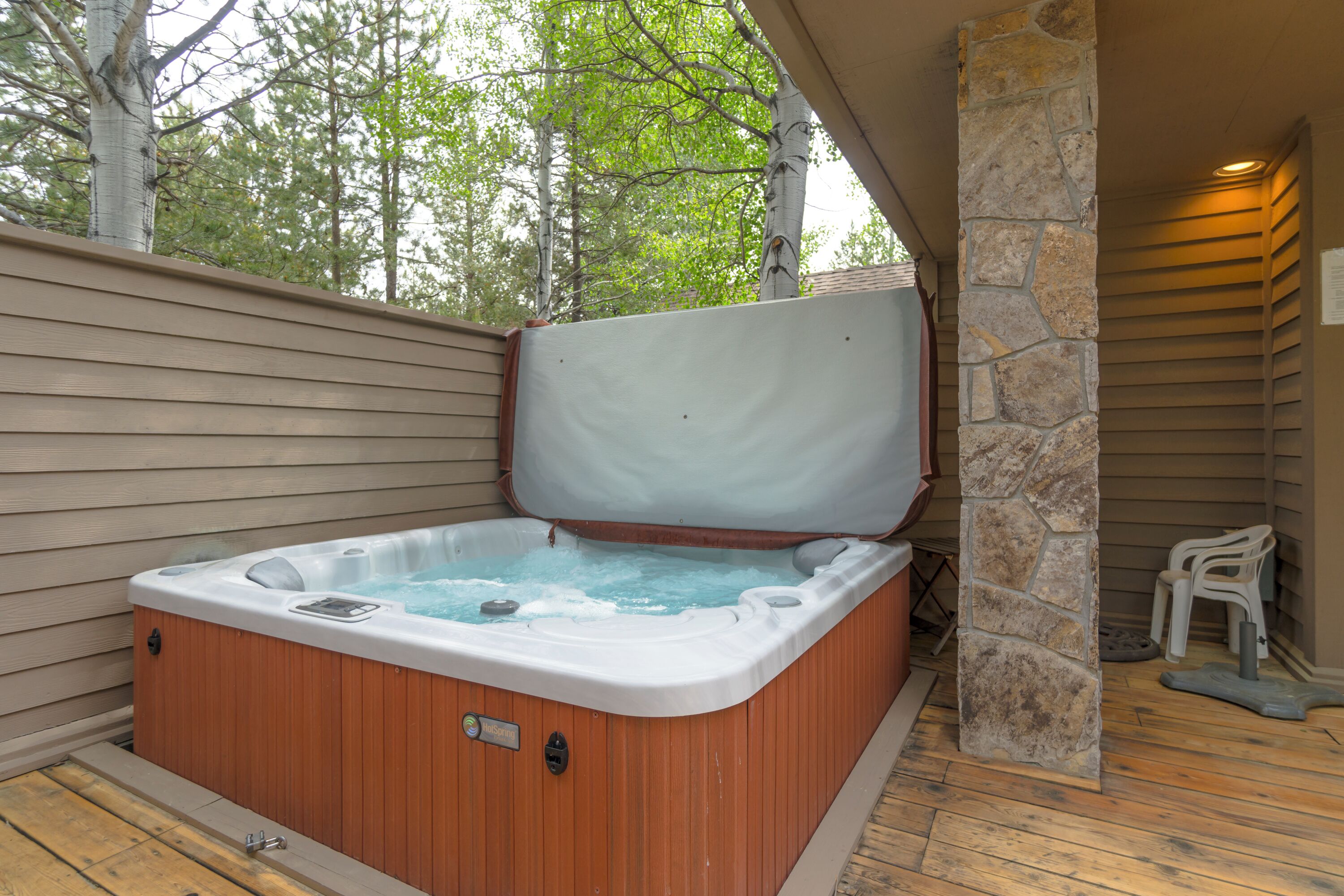 Un jacuzzi con un pilar de piedra y cubierta de madera, rodeado de árboles.