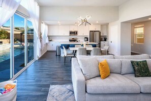 A modern kitchen with white cabinets, stainless steel appliances, and a dining area with a blue tablecloth. - @ Marbella Lane - Desert Dream Pool/spa & Games (Desert Hot Springs)