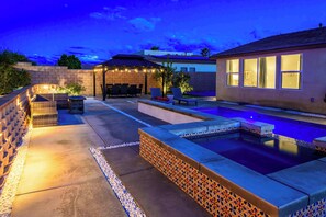A backyard with a swimming pool, outdoor seating, and a covered patio area. - @ Marbella Lane - Desert Dream Pool/spa & Games (Desert Hot Springs)