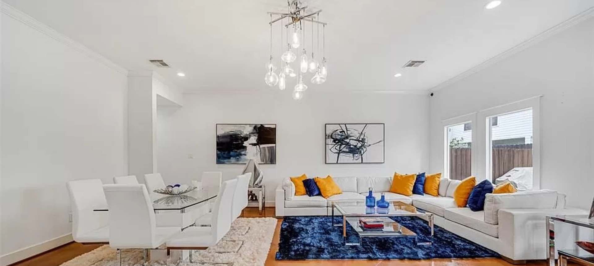 A modern living room with a dining area, white furniture, a chandelier, and artwork on the walls.