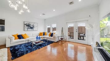 A spacious living room with a white sofa, blue rug, and a large window.