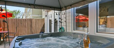 A hot tub with a glass and bottle, a wooden fence, and a patio umbrella.