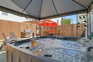 A hot tub with a bottle of wine, a glass, and a red umbrella in a backyard setting. - 3BR Home With Power, Wifi & Hot Tub (Houston)