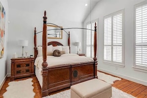 A four-poster bed with a wooden frame, a bedside table with drawers, a round mirror, and a white rug. - 3BR Home With Power, Wifi & Hot Tub (Houston)
