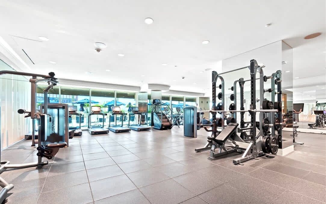Ein modernes Fitnessstudio mit unterschiedlicher Trainingsausstattung, darunter Laufbänder, Kraftgeräte und Kurzhanteln.