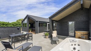 Une terrasse extérieure moderne comprenant un espace repas, un jacuzzi et un coin salon abrité.