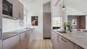 A modern kitchen with a central island, built-in appliances, and a view to the outdoors. - VillaVilla 958 - Skåstrup Strand, Fyn og øer (Bogense)