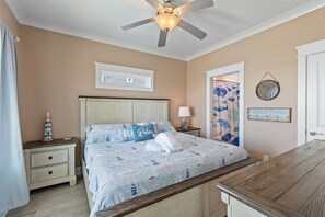 Ein Schlafzimmer mit Bett, Nachttisch, Lampe, Deckenventilator sowie einer Wand mit Spiegel und Schild.