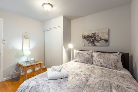 A bedroom with a floral-patterned bedspread, a bedside table with a lamp, and a wall-mounted artwork.