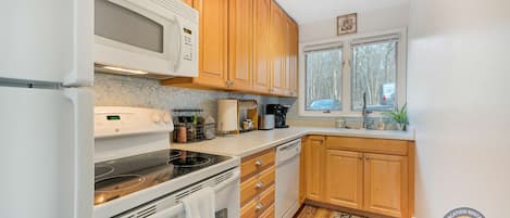 Une cuisine avec des meubles en bois, un four à micro-ondes, une cuisinière et une fenêtre donnant sur les arbres.