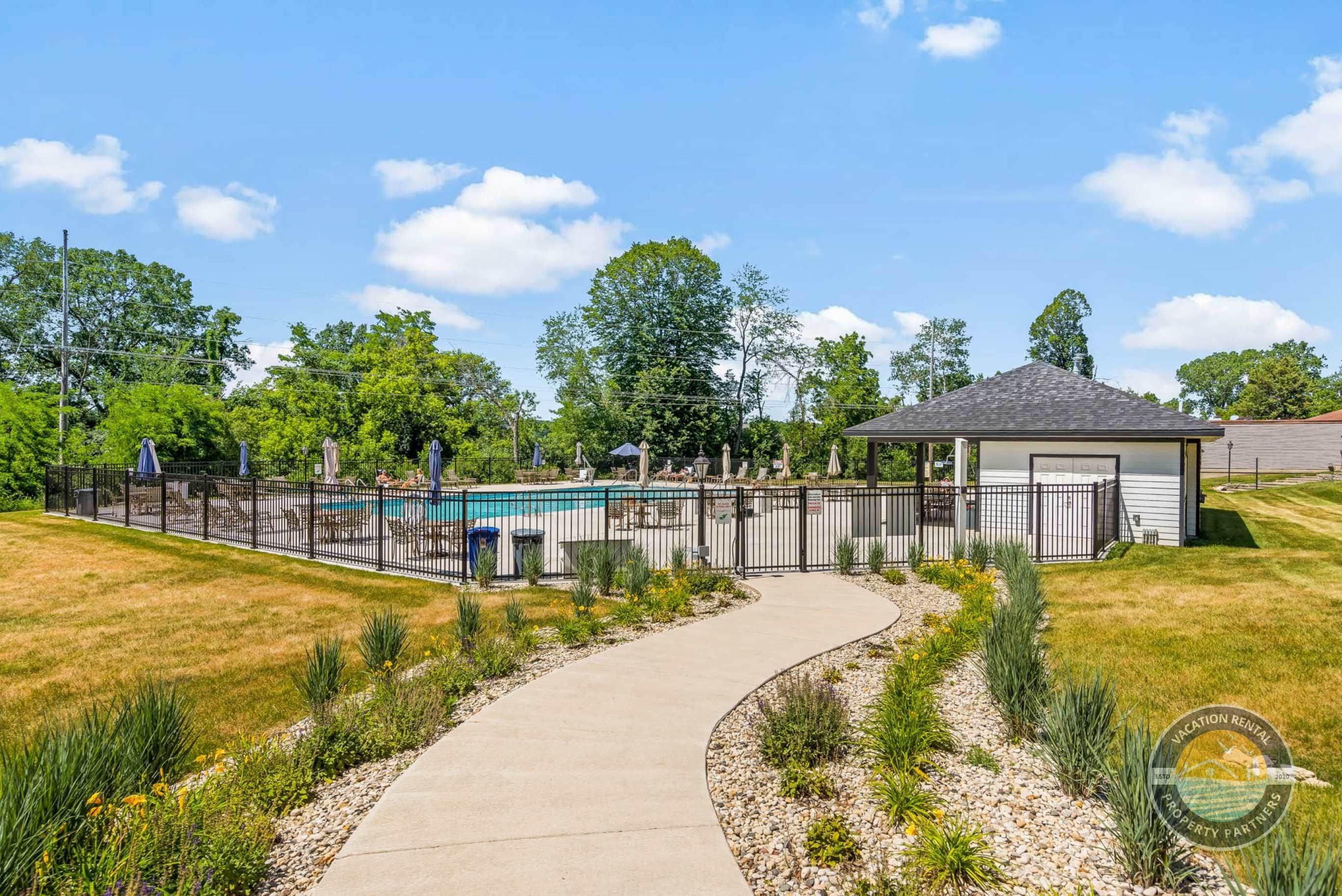 A fenced outdoor area with a pool, a gazebo, and a curved pathway.