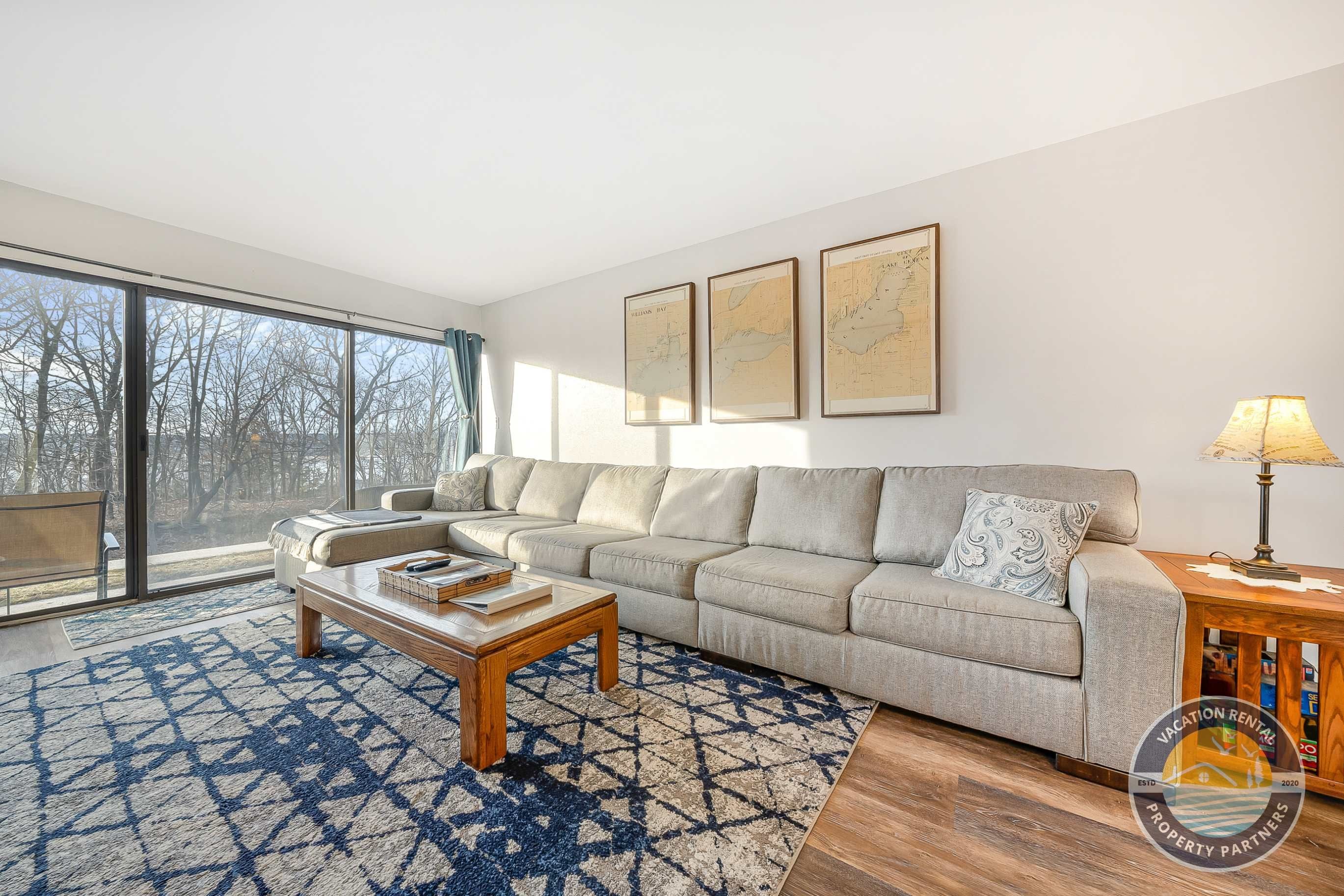 A modern living room with a sectional sofa, a coffee table, and a large window offering a view of trees.