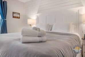 A neatly made bed with folded towels, a wall-mounted sign reading 'Lake House,' and a bedside lamp.