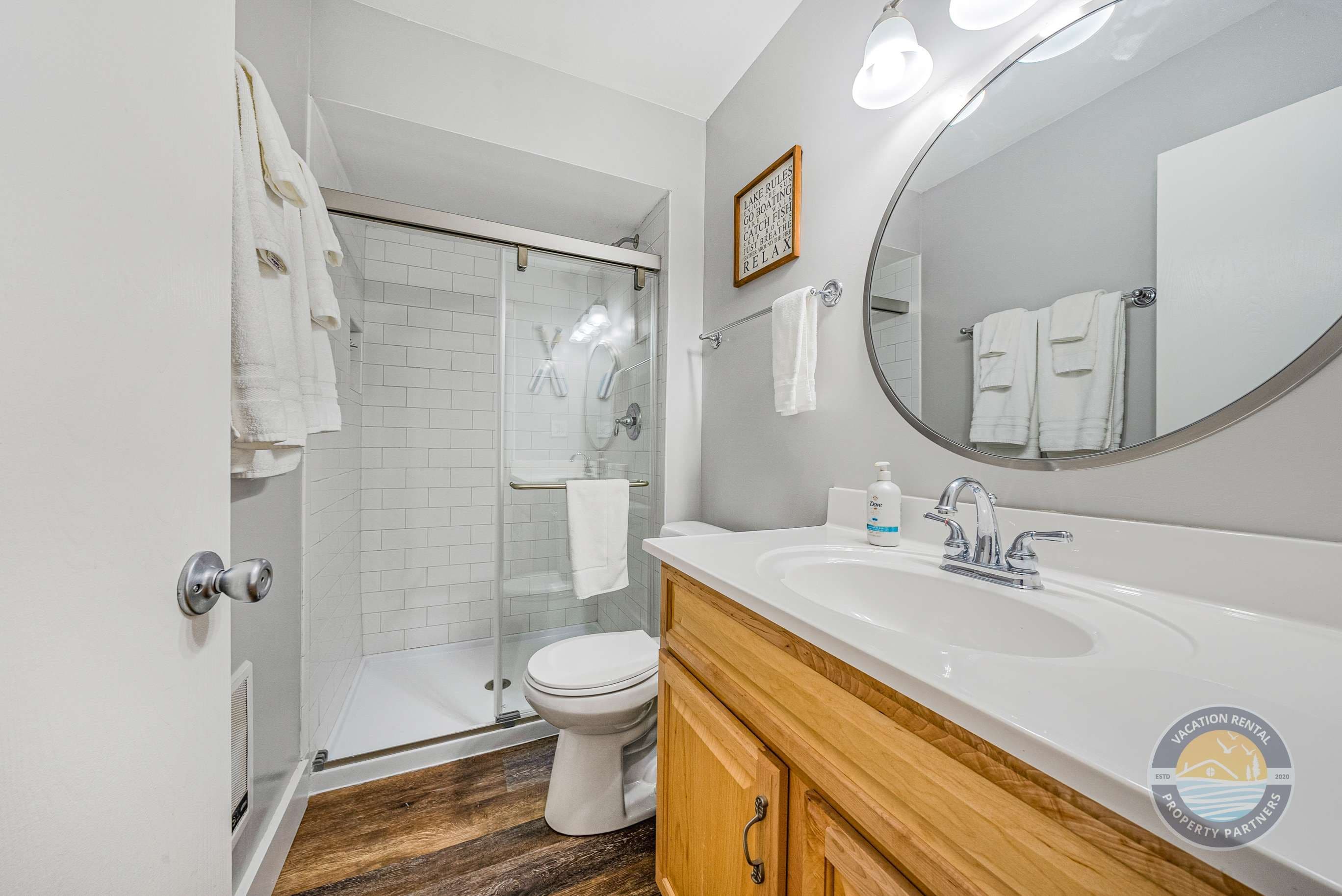 A bathroom with a shower, toilet, sink, and a large mirror.