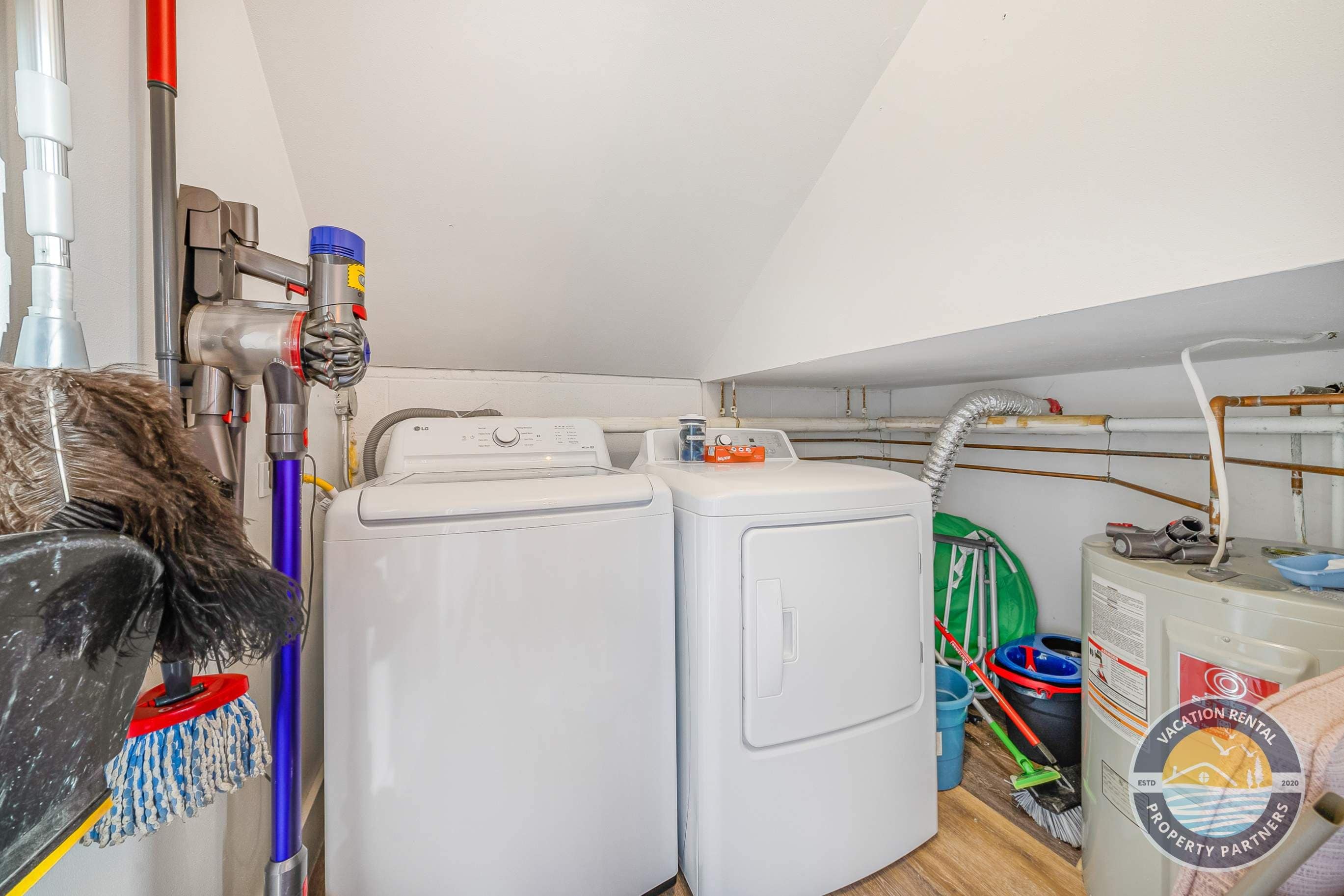 A laundry room with two white washing machines, a vacuum cleaner, and various cleaning supplies.
