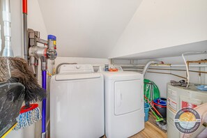 A laundry room with two white washing machines, a vacuum cleaner, and various cleaning supplies.