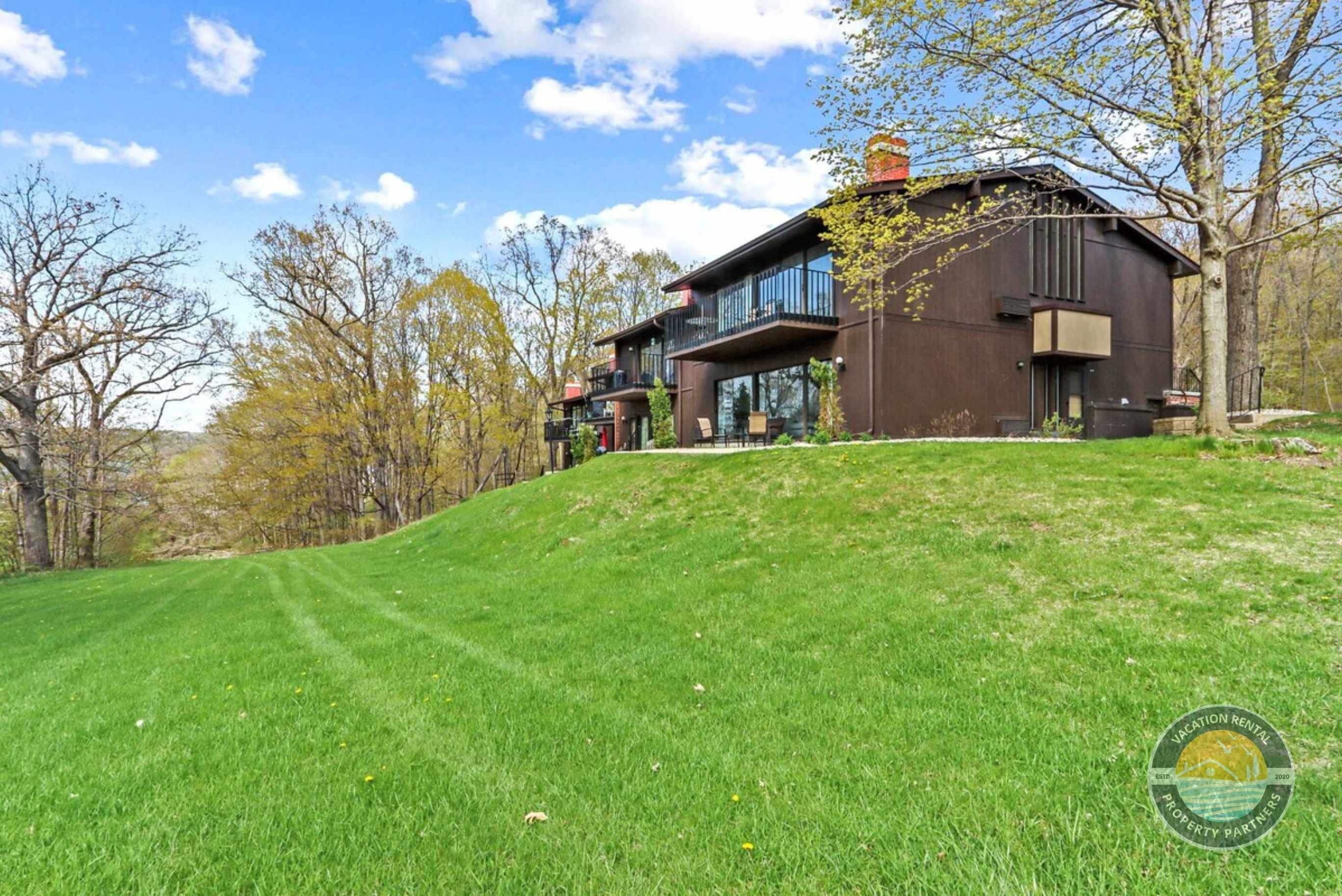 A modern two-story house with a large balcony, surrounded by a well-maintained lawn and trees.