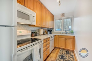 A kitchen with wooden cabinets, a microwave, stove, and a window with a view of trees.