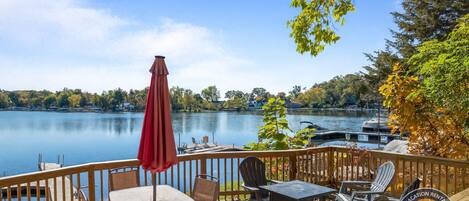 A wooden deck with outdoor furniture, a red umbrella, and a view of a lake with boats.