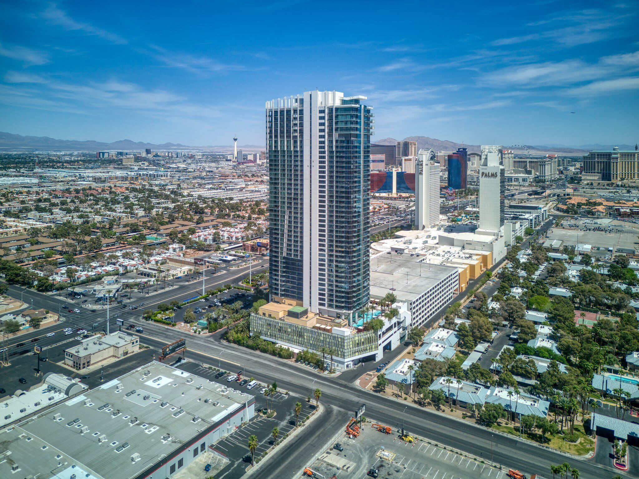 A high-rise building with a modern glass facade, surrounded by a mix of commercial and residential buildings, with a clear sky and distant mountains.