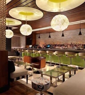 Una zona de bar con varios taburetes y un espacio de estar con mesas y sillas.
